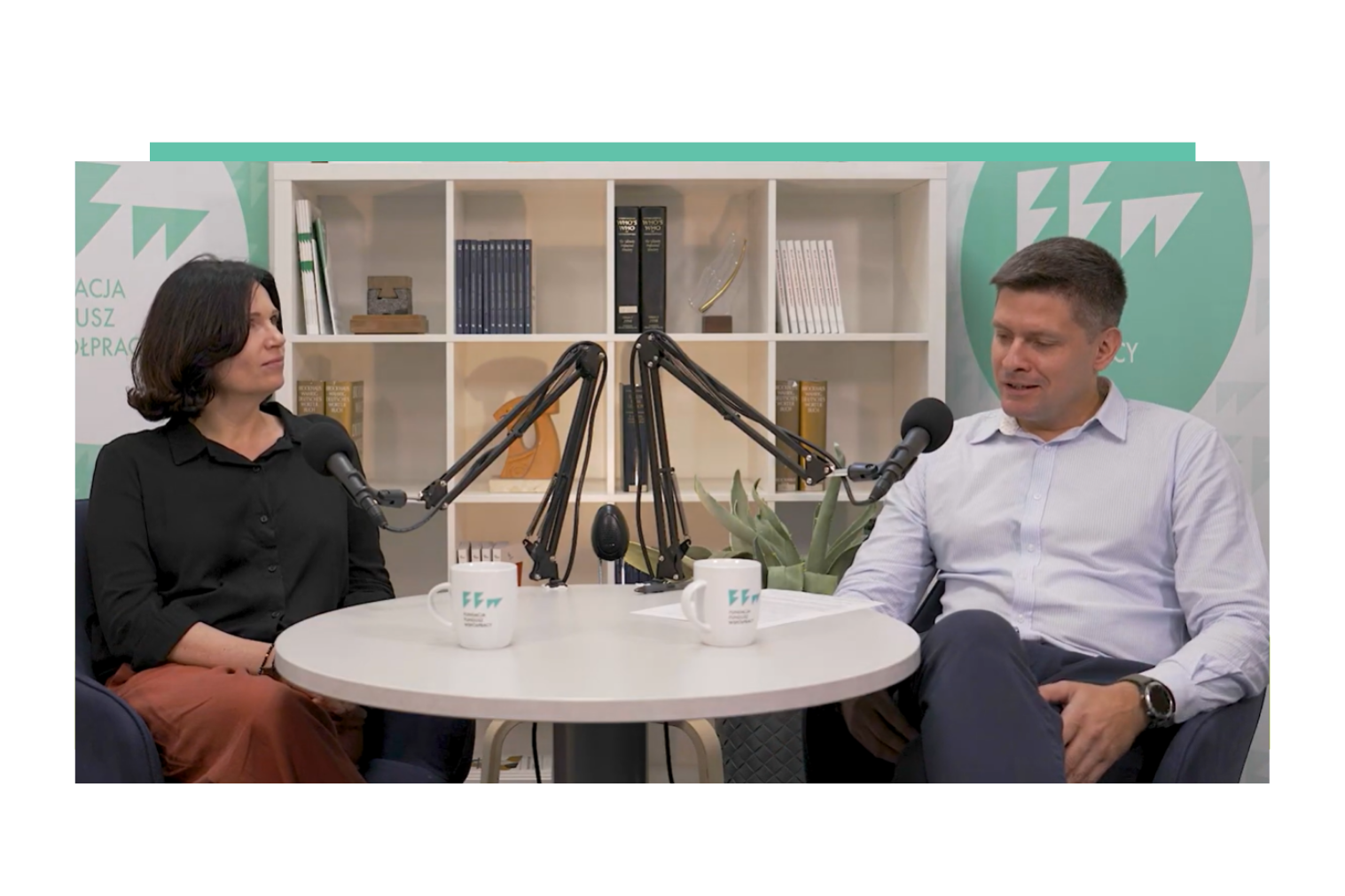 Dwie osoby siedzące w studio przy stole z mikrofonami